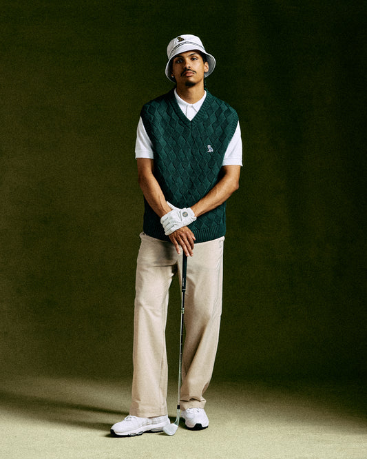 Midnight green basketweave sweater vest with V-neck worn over white t-shirt, paired with cream pants and golf accessories.