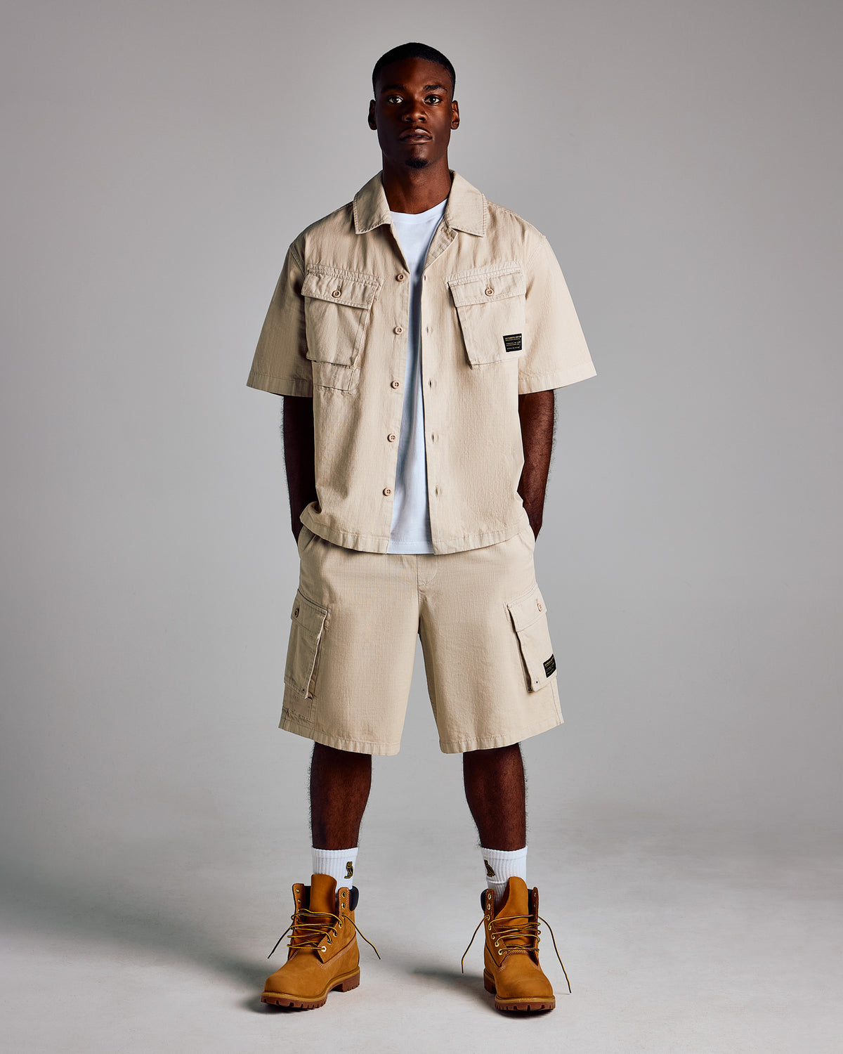 Beige cargo shorts with side pockets and button closure, styled on model.