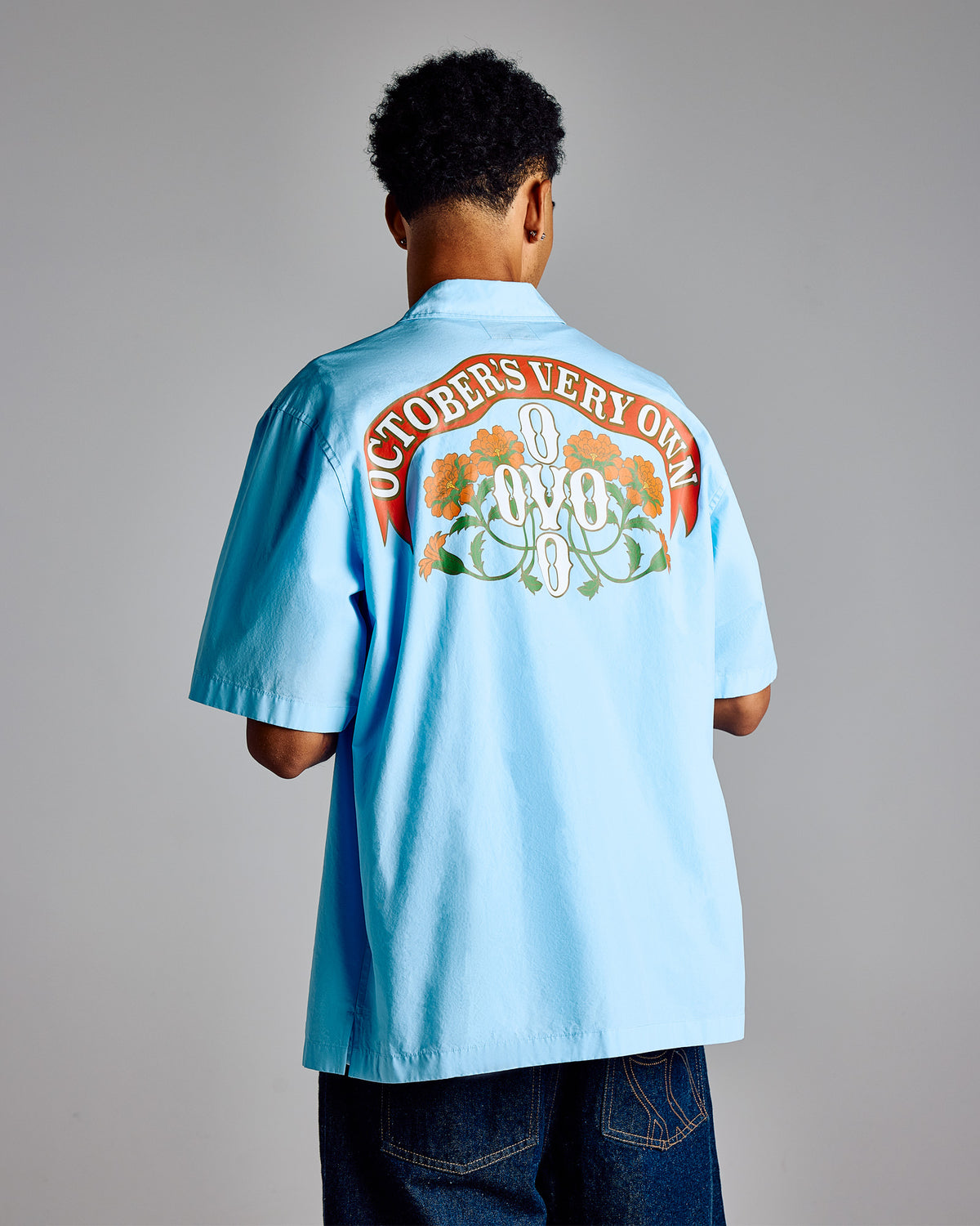 Light blue camp shirt with "October's Very Own" text and floral graphic on back.