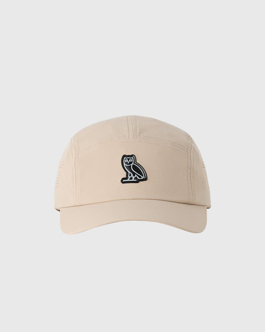 Sandstone five-panel cap with small black owl emblem on front.