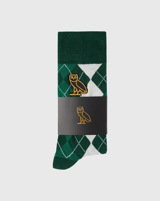 Green argyle sock with white diamond pattern and gold owl logo, displayed in packaging.