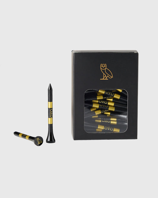 Black golf tees with gold stripes and OVO branding, displayed with packaging box featuring owl logo.
