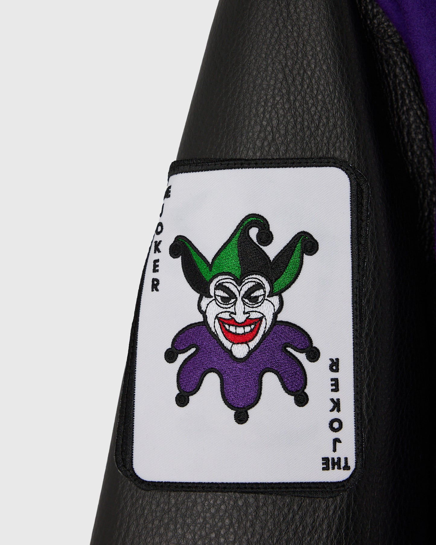 Black varsity jacket with white patch featuring Joker character illustration in green and purple with "JOKER" and "THE JOKER"