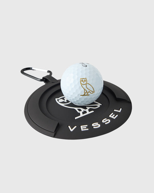 Black Vessel putting disc with white golf ball featuring gold owl logo resting on concentric circular base.
