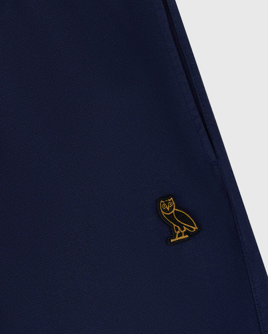 Navy sweatpant with small gold owl embroidery on thigh, ribbed fabric texture visible.