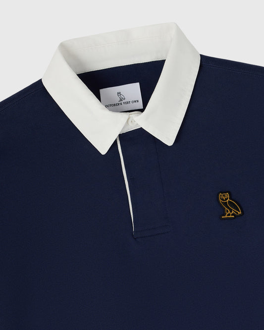 Navy rugby polo with white collar and gold owl embroidered logo on chest.