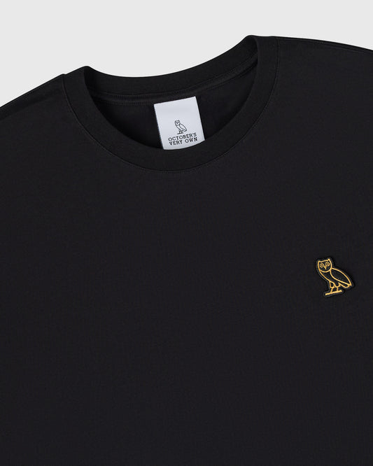 Black crew neck t-shirt with small gold owl embroidered on chest and white brand label inside collar.