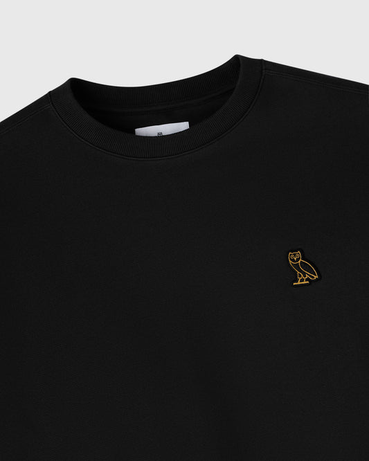 Black crewneck sweatshirt with small gold owl embroidery on chest.