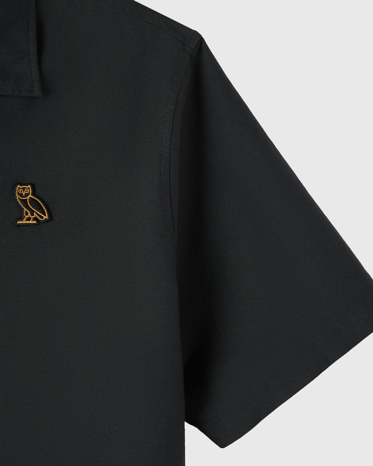 Black camp shirt with gold owl embroidery on chest pocket and short sleeves.