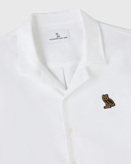 White oxford camp shirt with embroidered owl logo on chest and brand label on interior neckline.