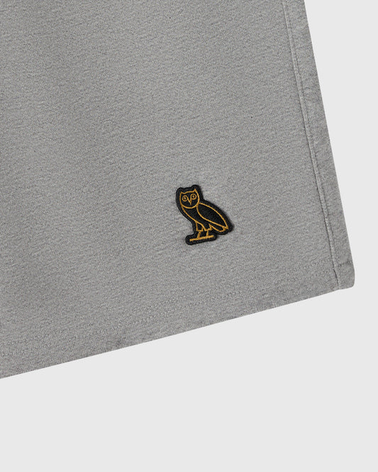 Heather grey sweatshort with small black and gold owl embroidered patch on thigh.