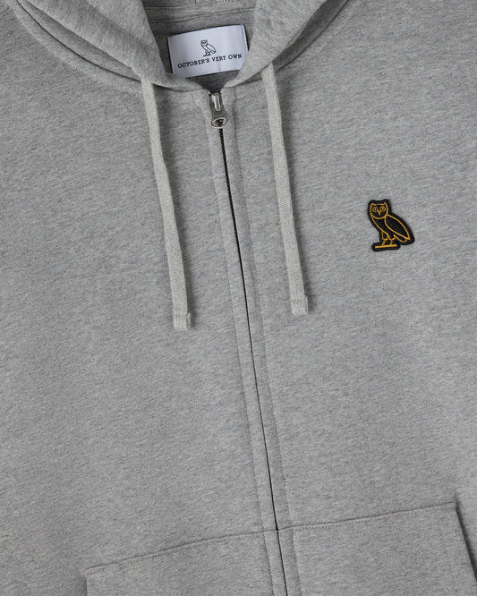 Heather grey full-zip hoodie with drawstrings, gold owl embroidery on chest, and brand label visible at neckline.