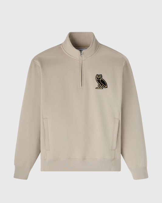 Beige quarter-zip mockneck sweatshirt with small black owl emblem on chest and front pockets.