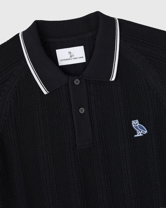 Black open knit polo sweater with white striped collar and small embroidered owl logo on chest.