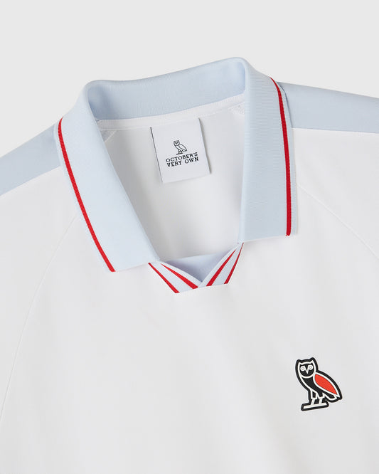 White piqué polo shirt with red and light blue striped collar and owl logo on chest.