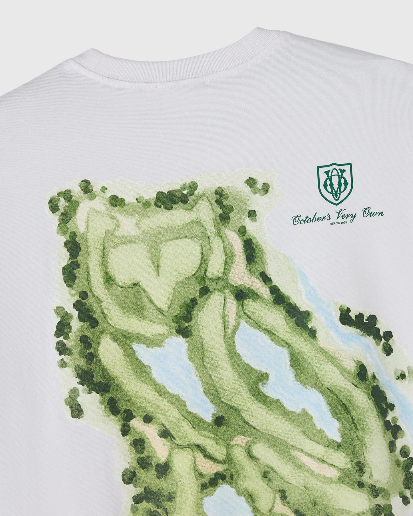 White t-shirt with green golf course layout forming an owl face design and OVO logo on chest.