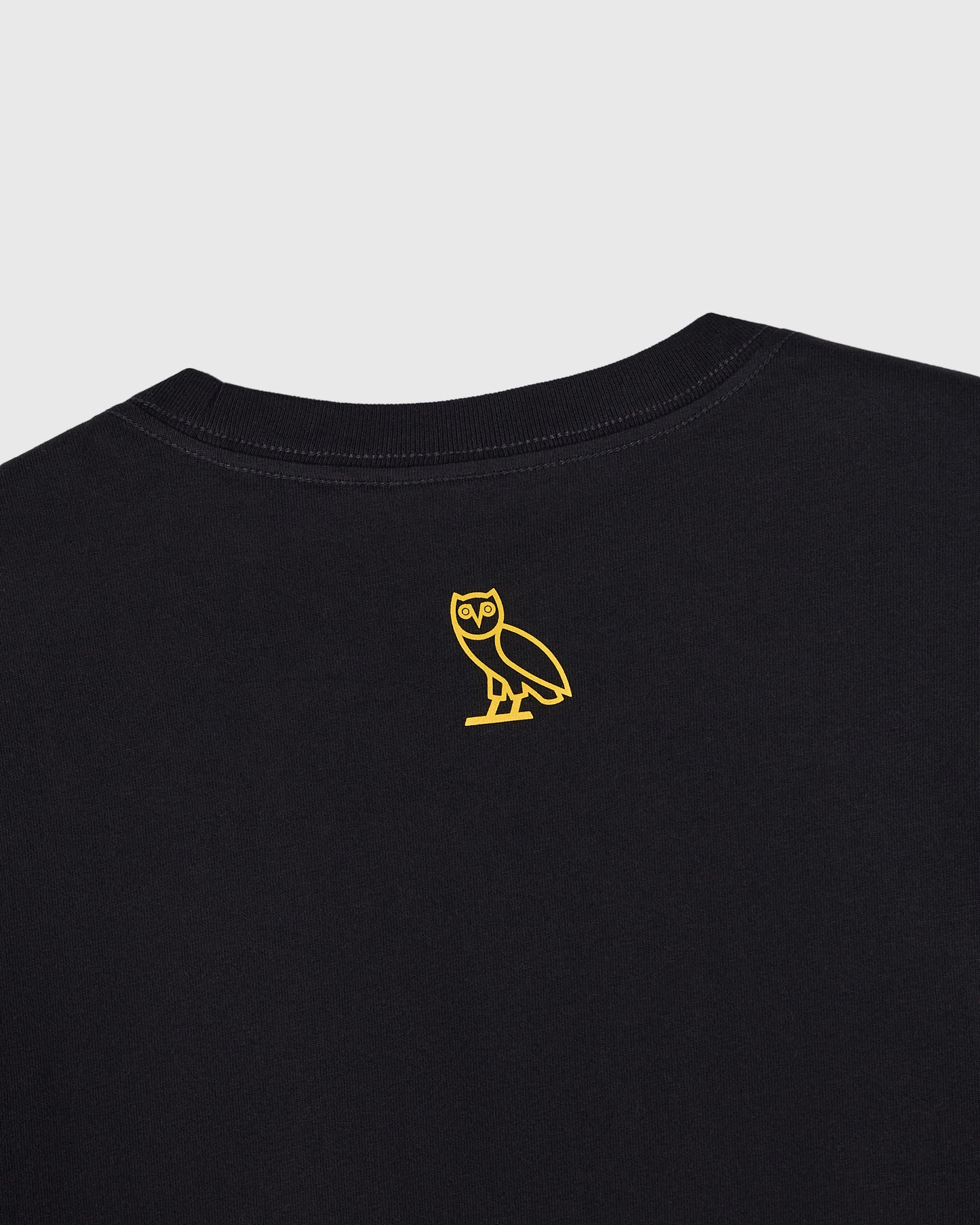 Black crewneck t-shirt with small yellow owl outline graphic on chest.