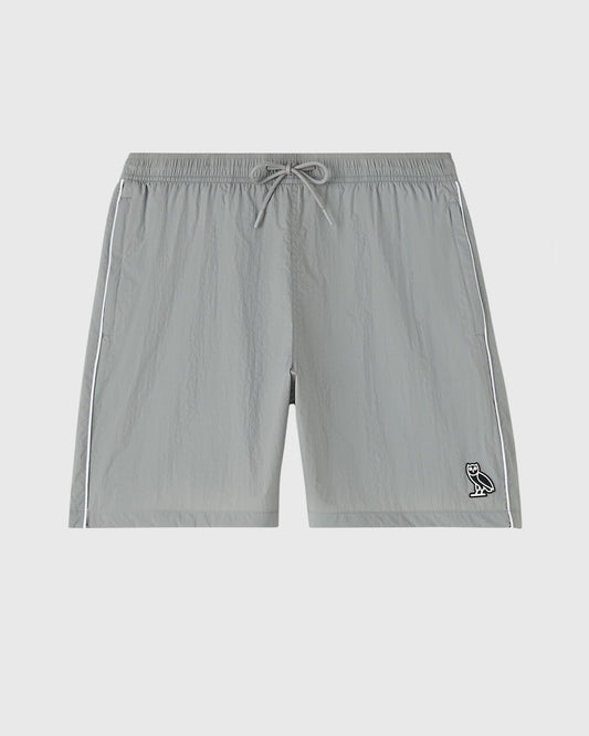 Cool grey nylon track shorts with drawstring waist, side stripes, and small owl logo on lower right leg.