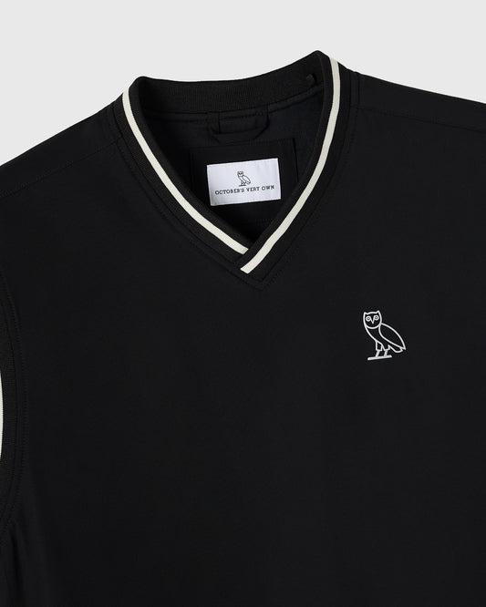 Black pullover vest with white stripe trim at V-neckline and owl logo embroidered on chest.