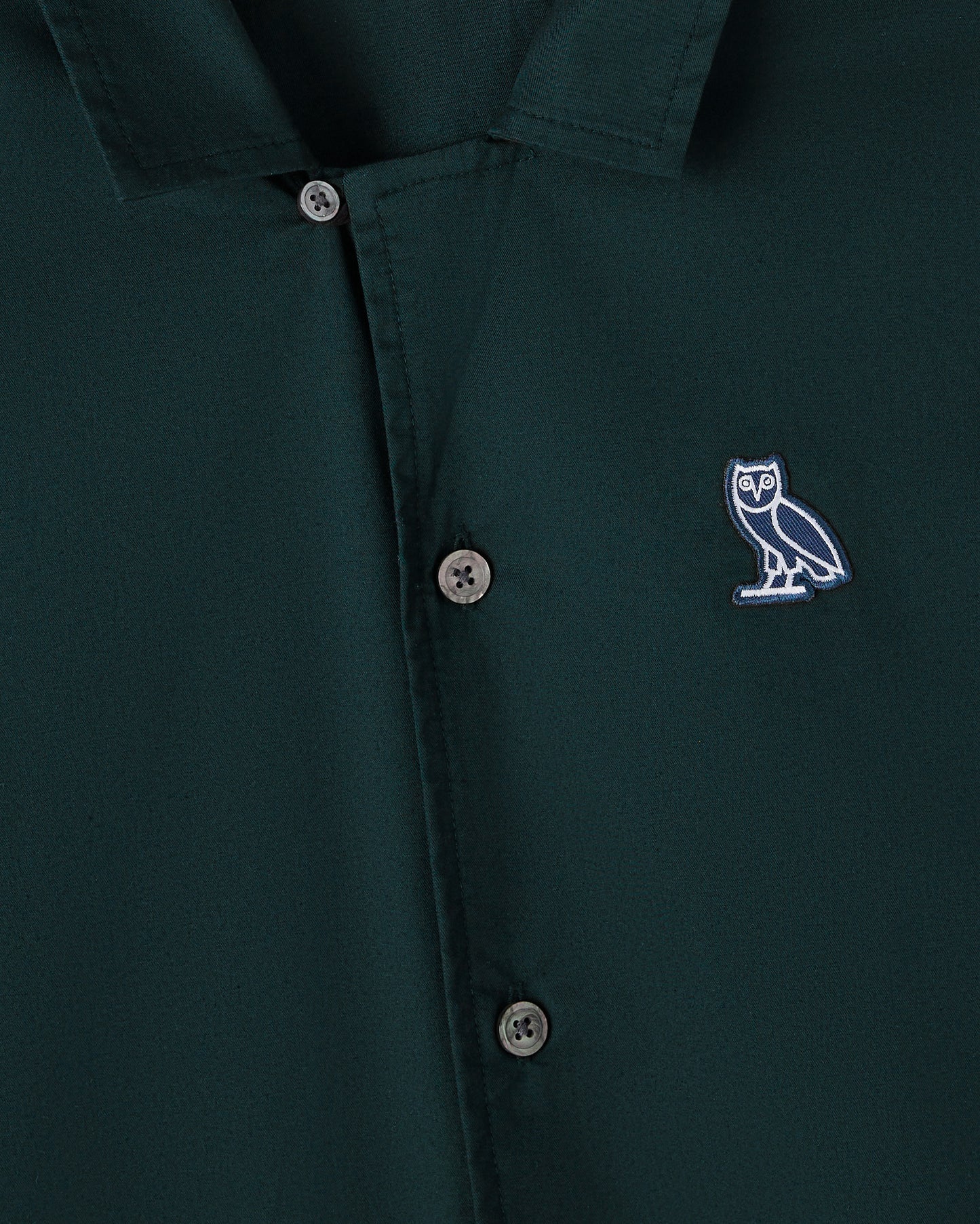 Midnight green camp shirt with owl embroidered logo and button-front closure.
