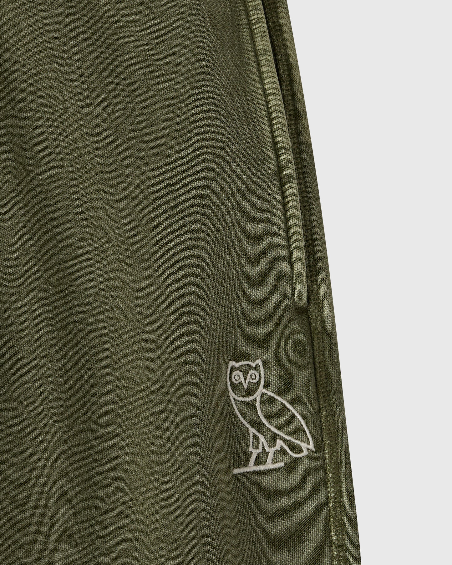 Cypress green sweatpant with ribbed texture and small white owl embroidery on leg.