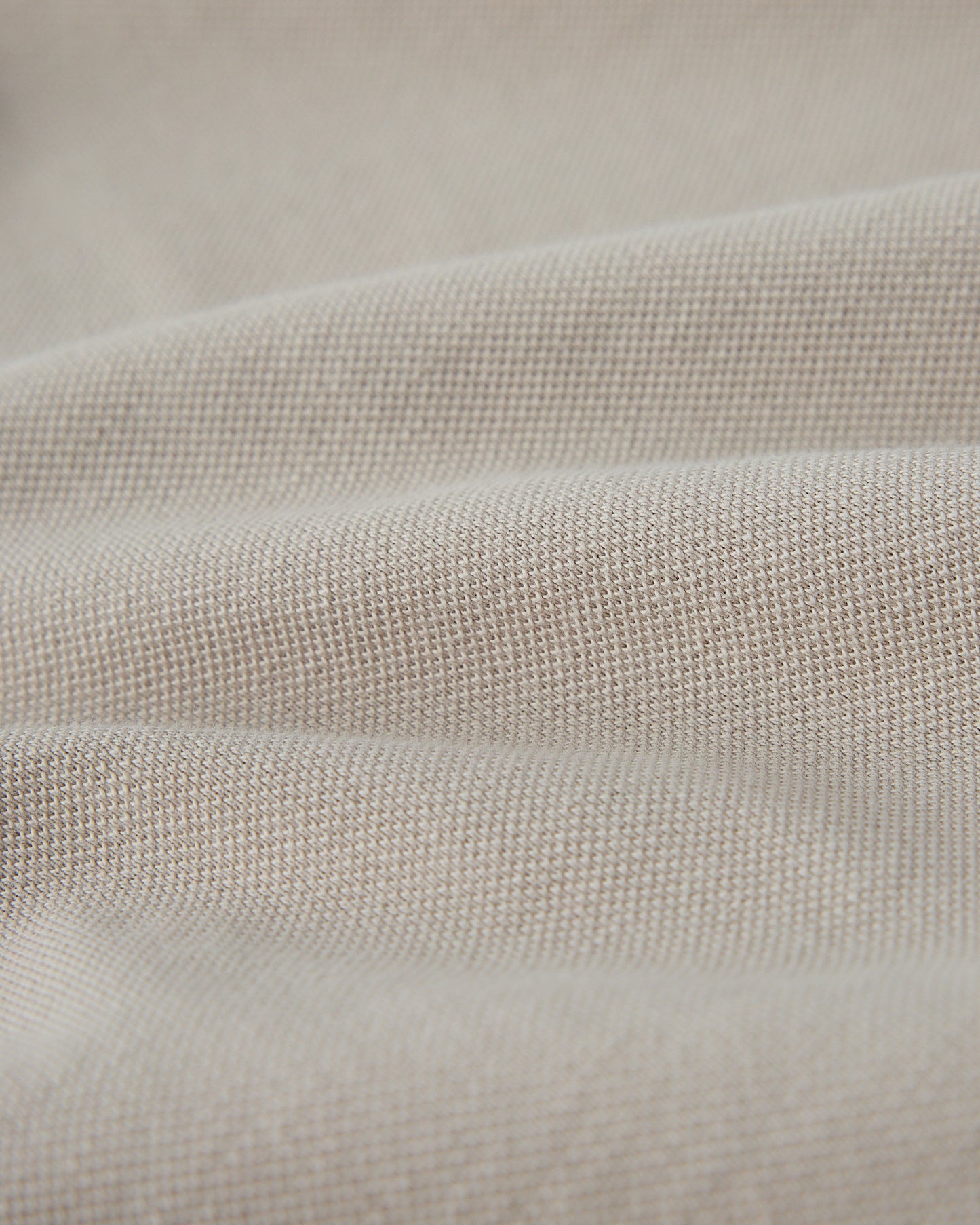 Close-up of sandstone-colored polo fabric showing textured knit weave.