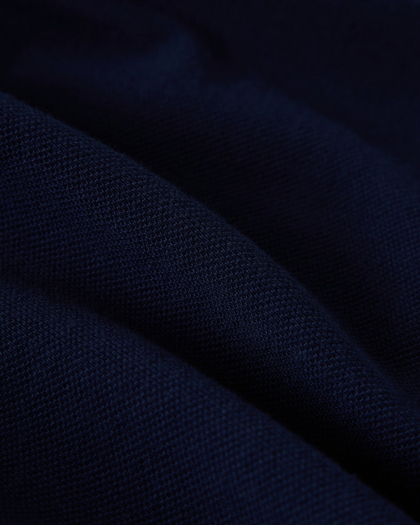 Navy blue polo shirt fabric with ribbed knit texture and diagonal fold detail.