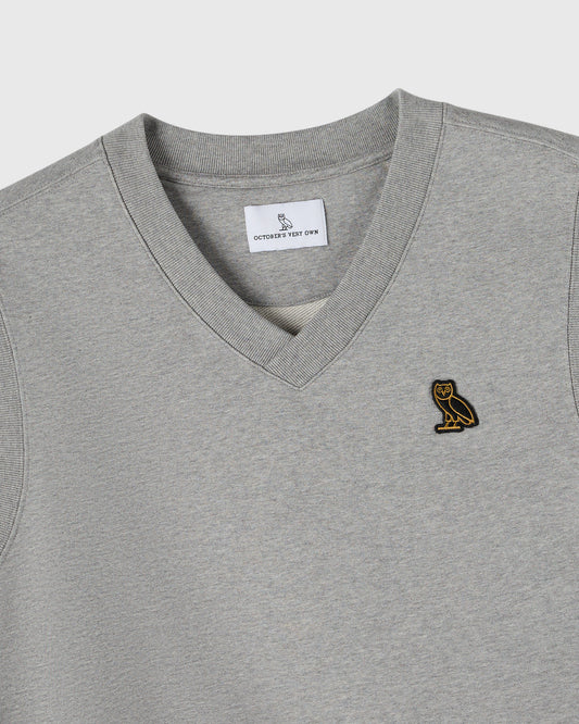 Heather grey v-neck vest with small gold owl embroidered on chest and brand label visible at neckline.