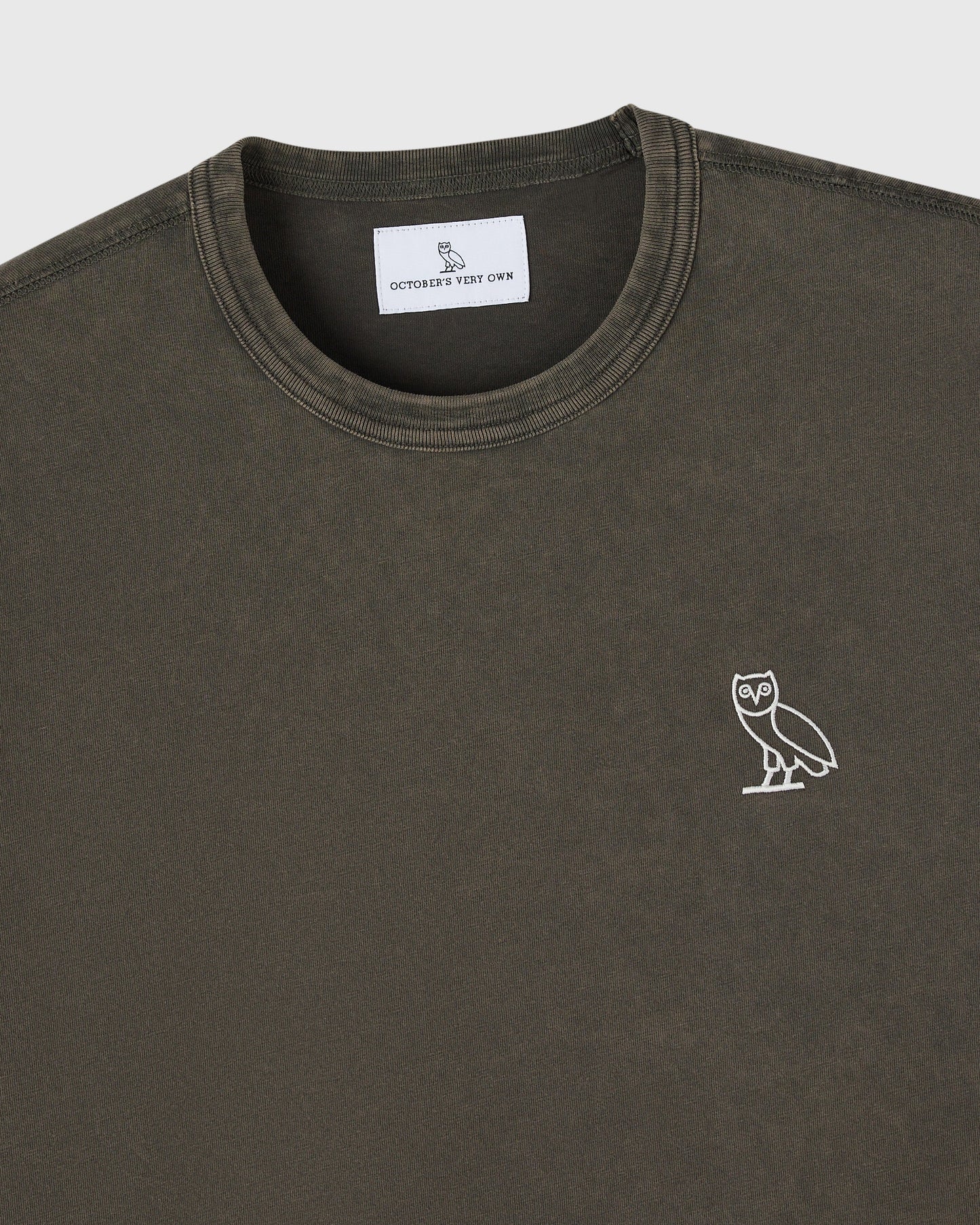 Deep olive crewneck t-shirt with small white owl embroidery on chest and brand label at neckline.