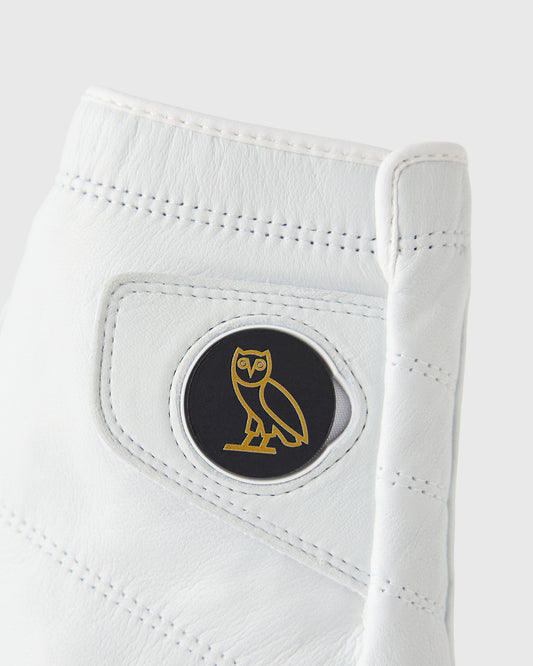 White leather golf glove with perforated details and circular black and gold owl logo on palm.
