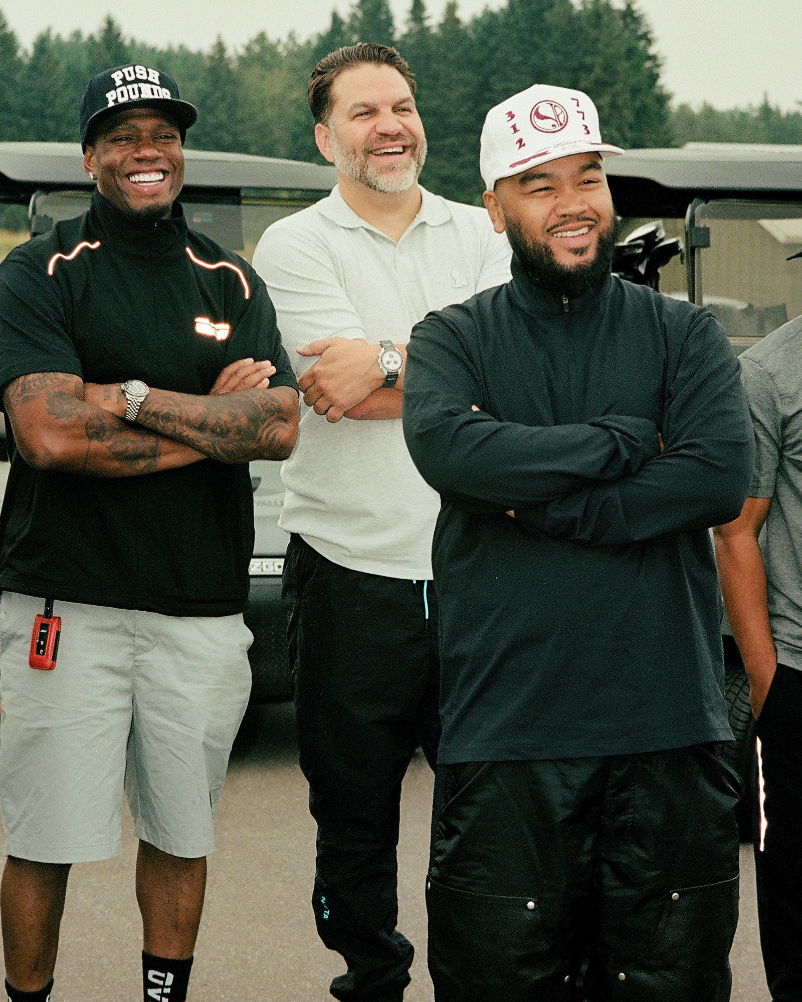 Three men standing together outdoors with trees in the background