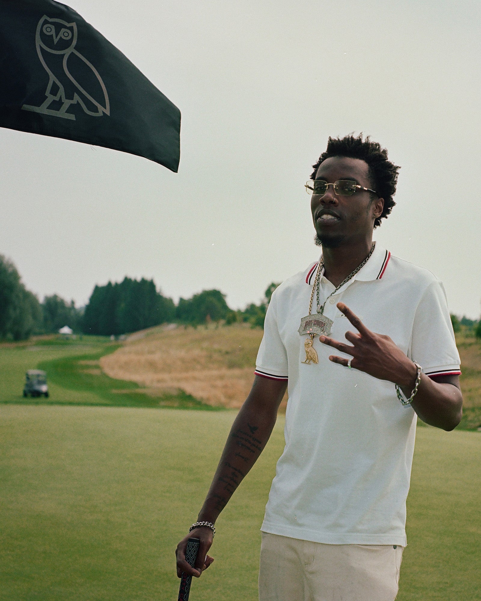Roy Woods on a golf course with a October's Very Own flag featuring an owl logo in the background