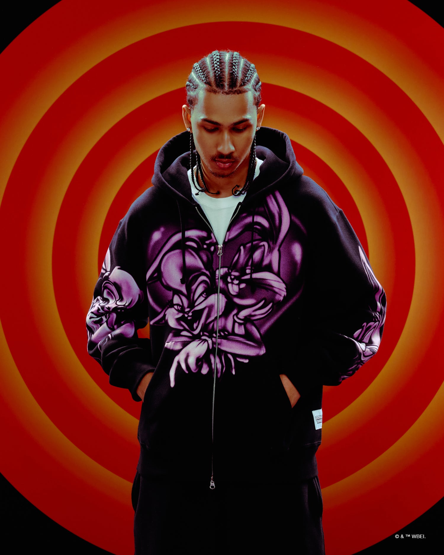 Person wearing a black October's Very Own x Looney Tunes hoodie with a purple floral design on an orange and red spiral background