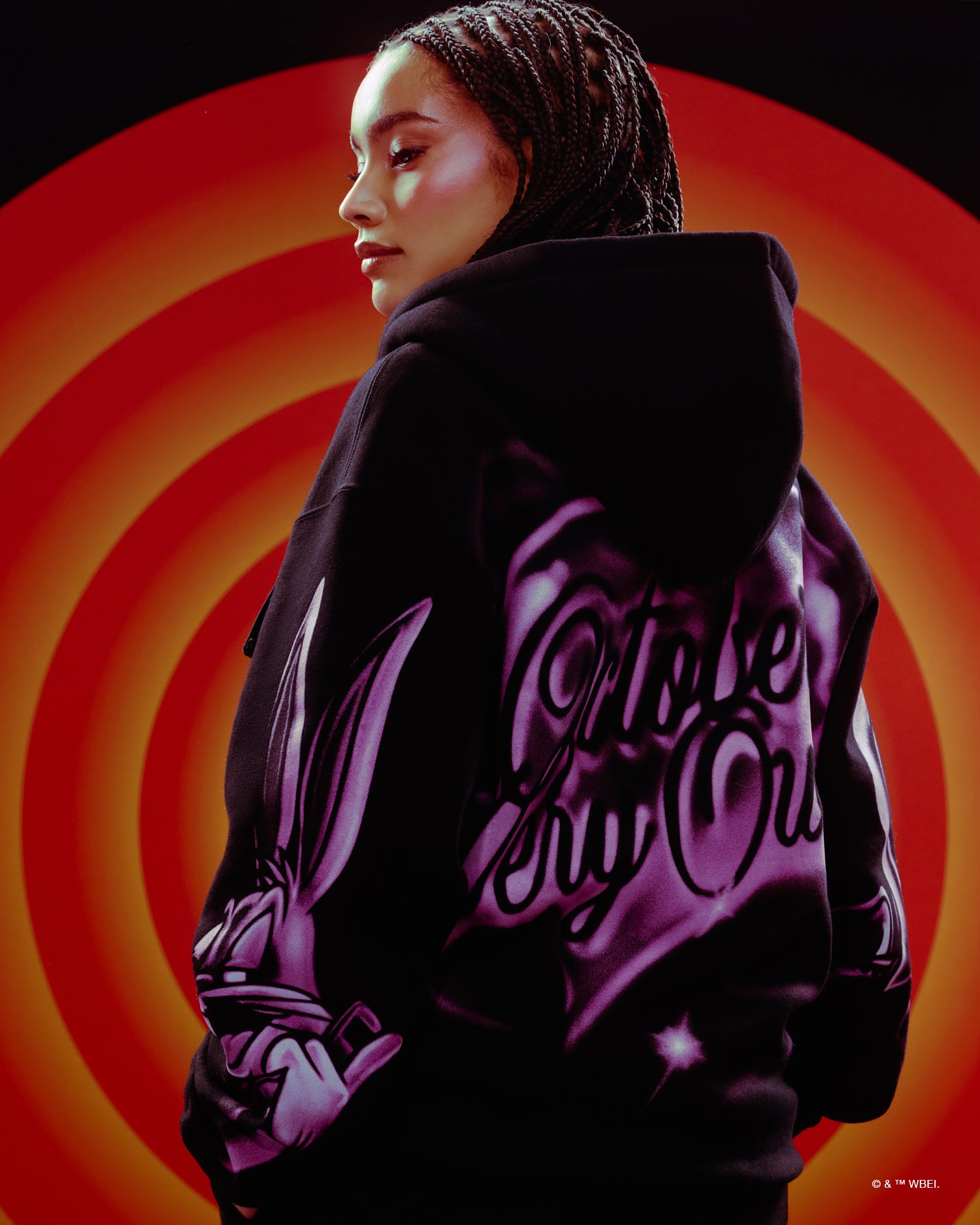 Person wearing a black October's Very Own x Looney Tunes hoodie with text on a red and orange circular background