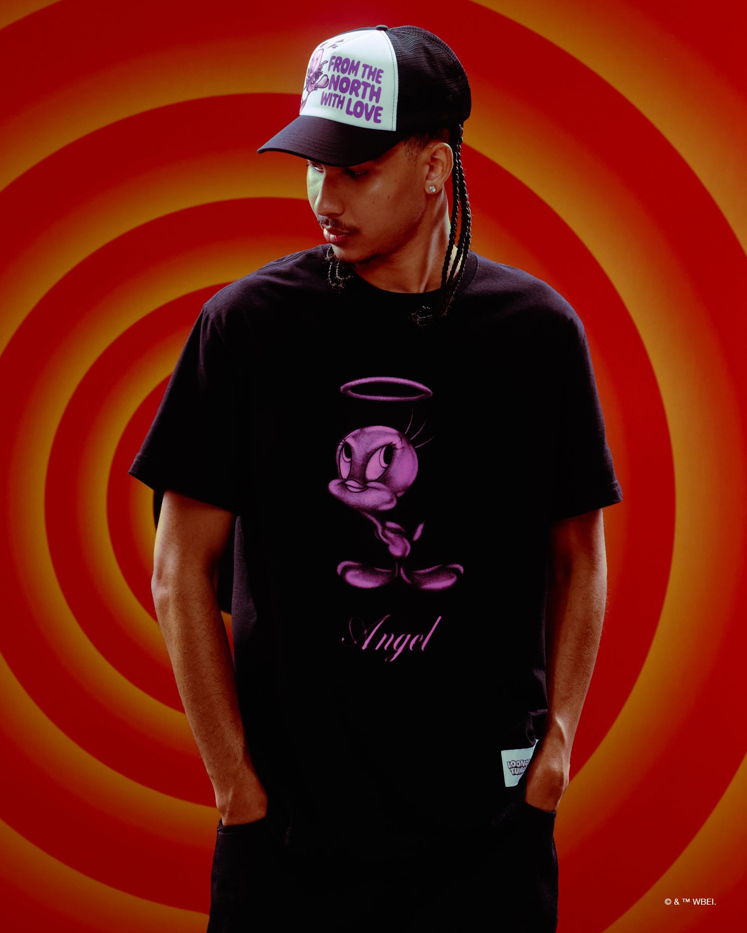 Person wearing a black October's Very Own x Looney Tunes t-shirt with a graphic design and a cap against an orange and red spiral background
