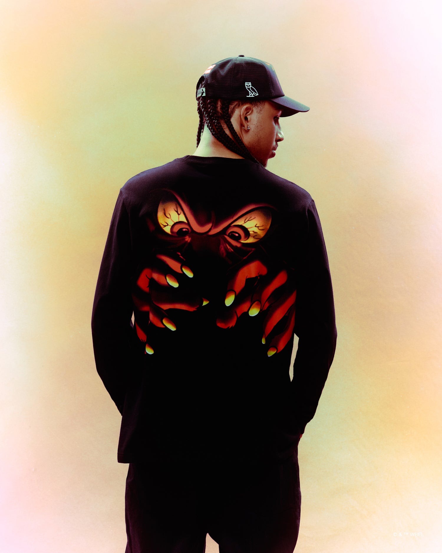 Person wearing a black October's Very Own x Looney Tunes hoodie with a colorful design on a gradient background