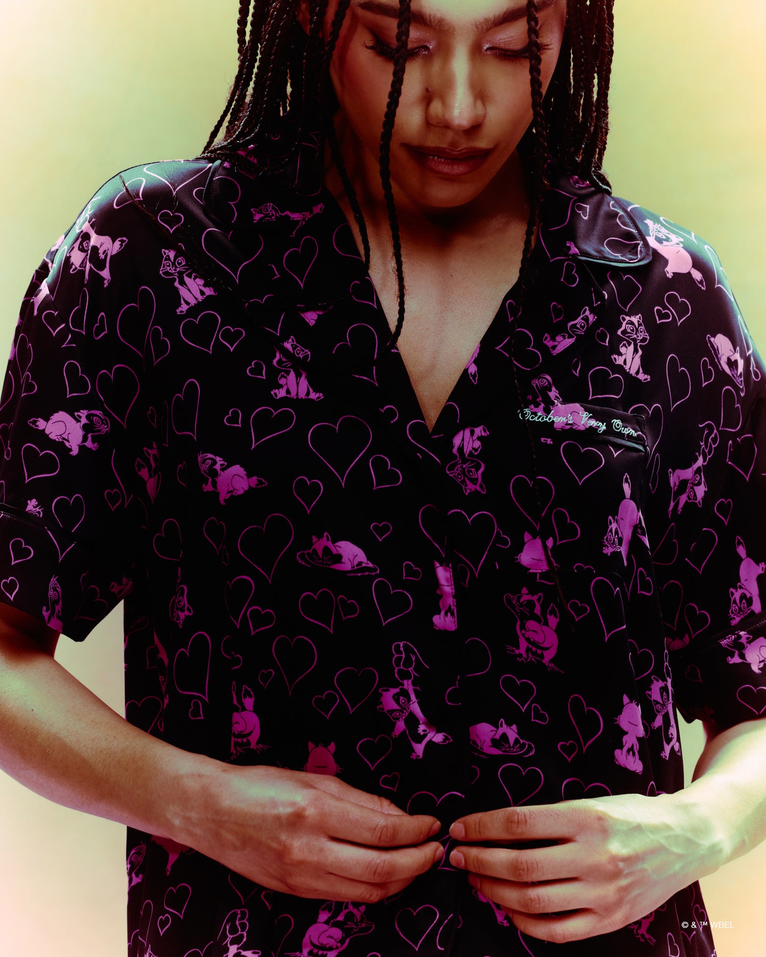 Person wearing a black October's Very Own x Looney Tunes shirt with pink heart and animal pattern against a yellow background