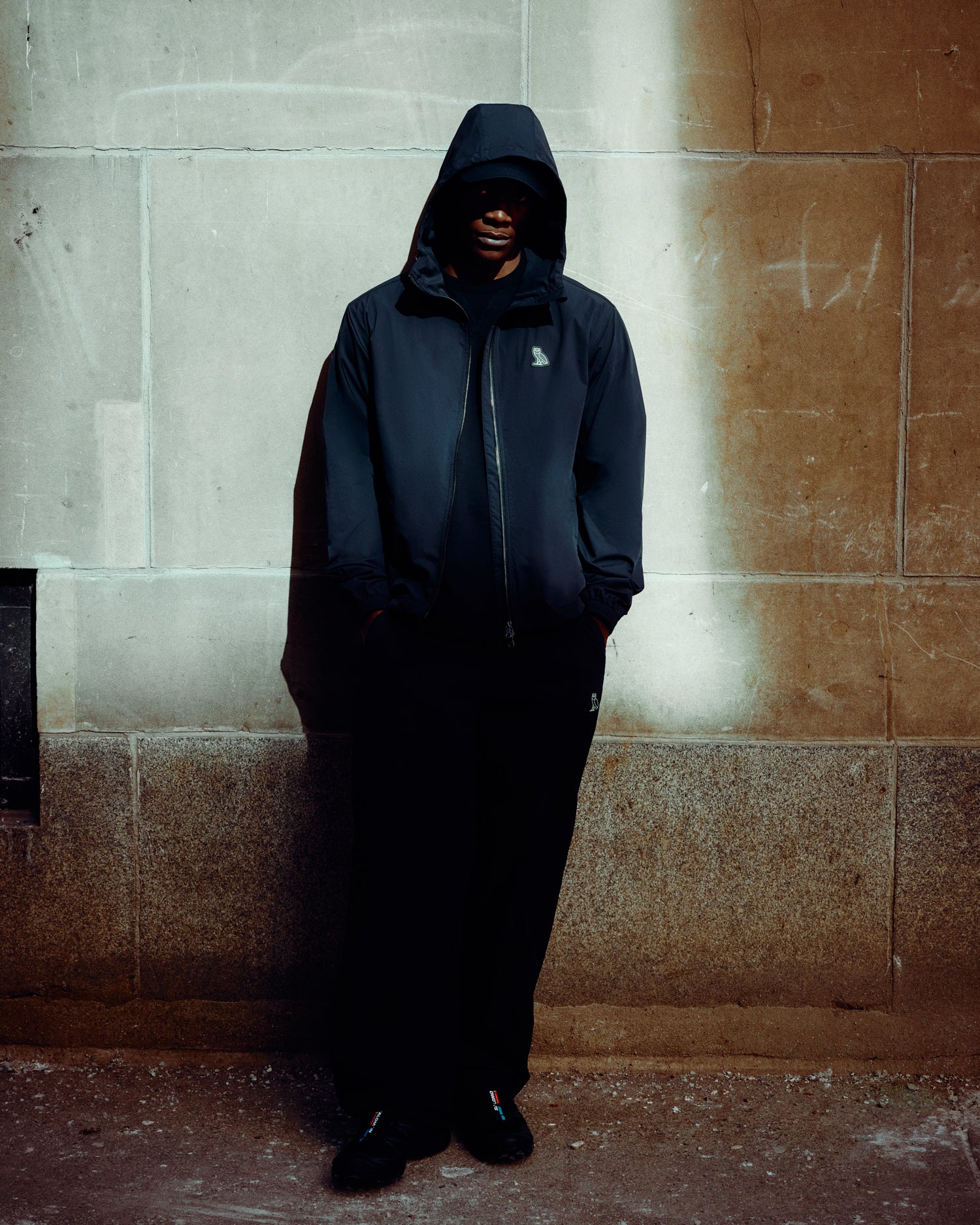 Person wearing a black October's Very Own raincoat standing against a stone wall.