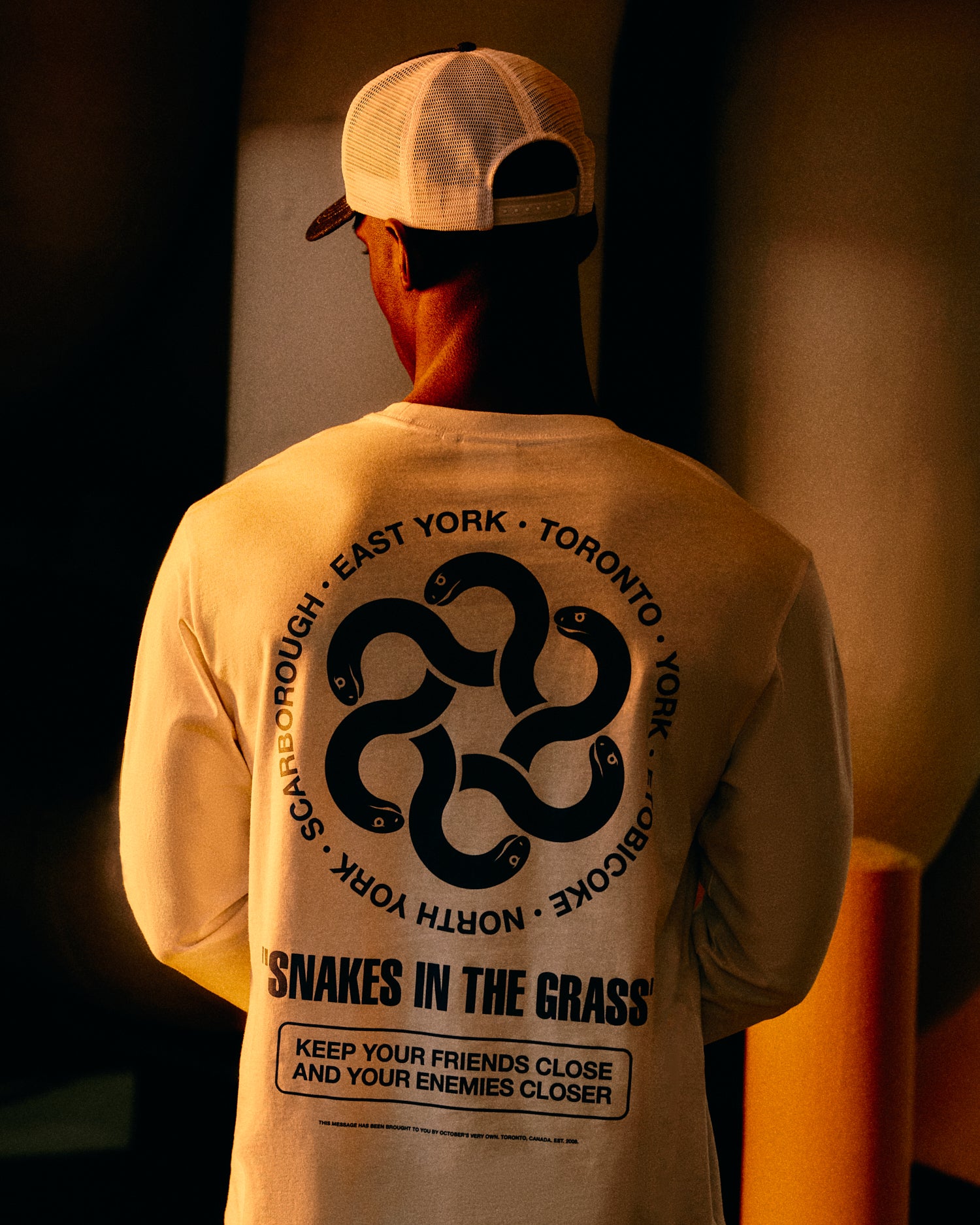 Person wearing a long-sleeve October's Very own t-shirt with a snake design and text on the back, standing against a dark background.