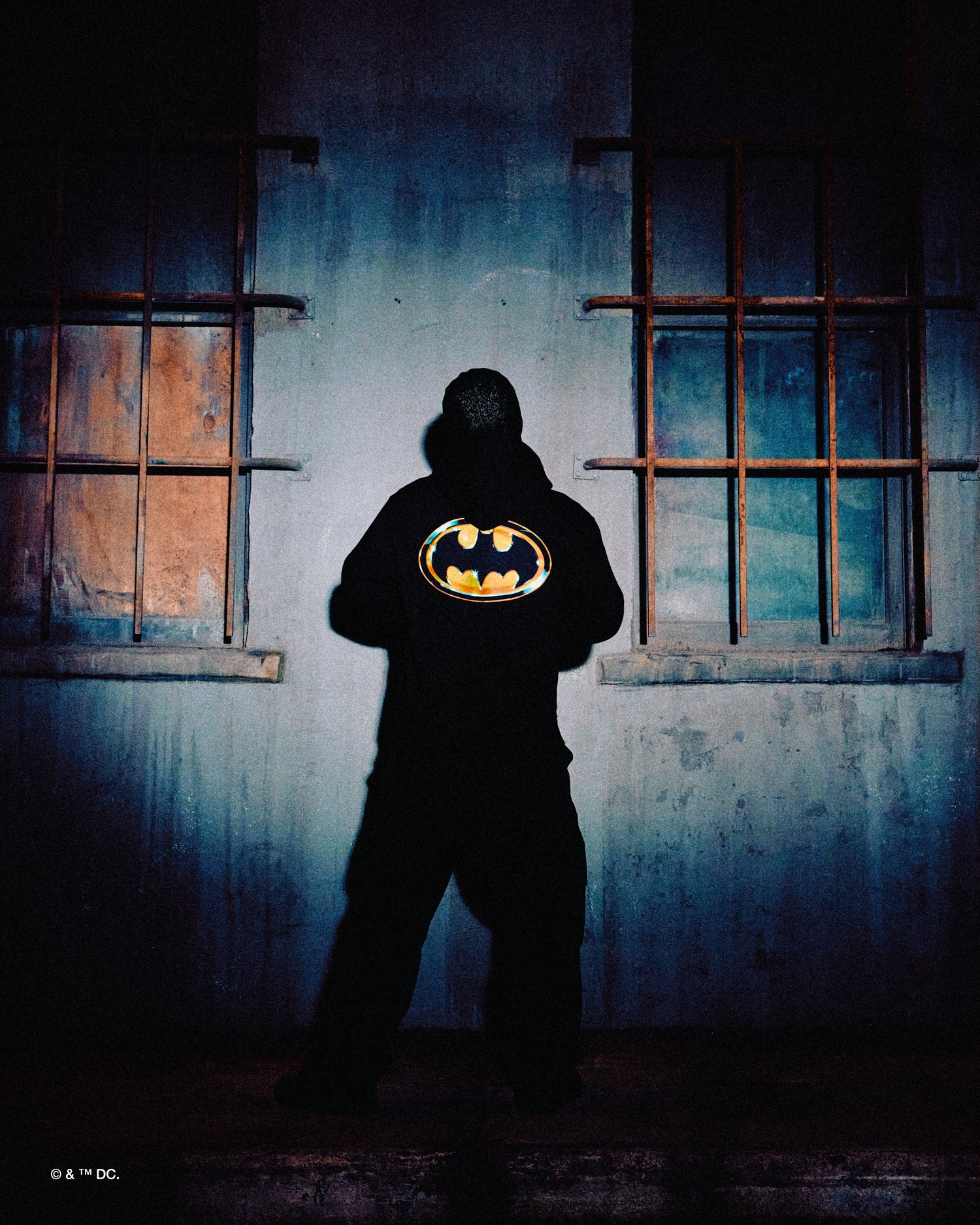 Person wearing a October's very Own x Batman x The Joker hoodie with a Batman logo in a dark, eerie setting
