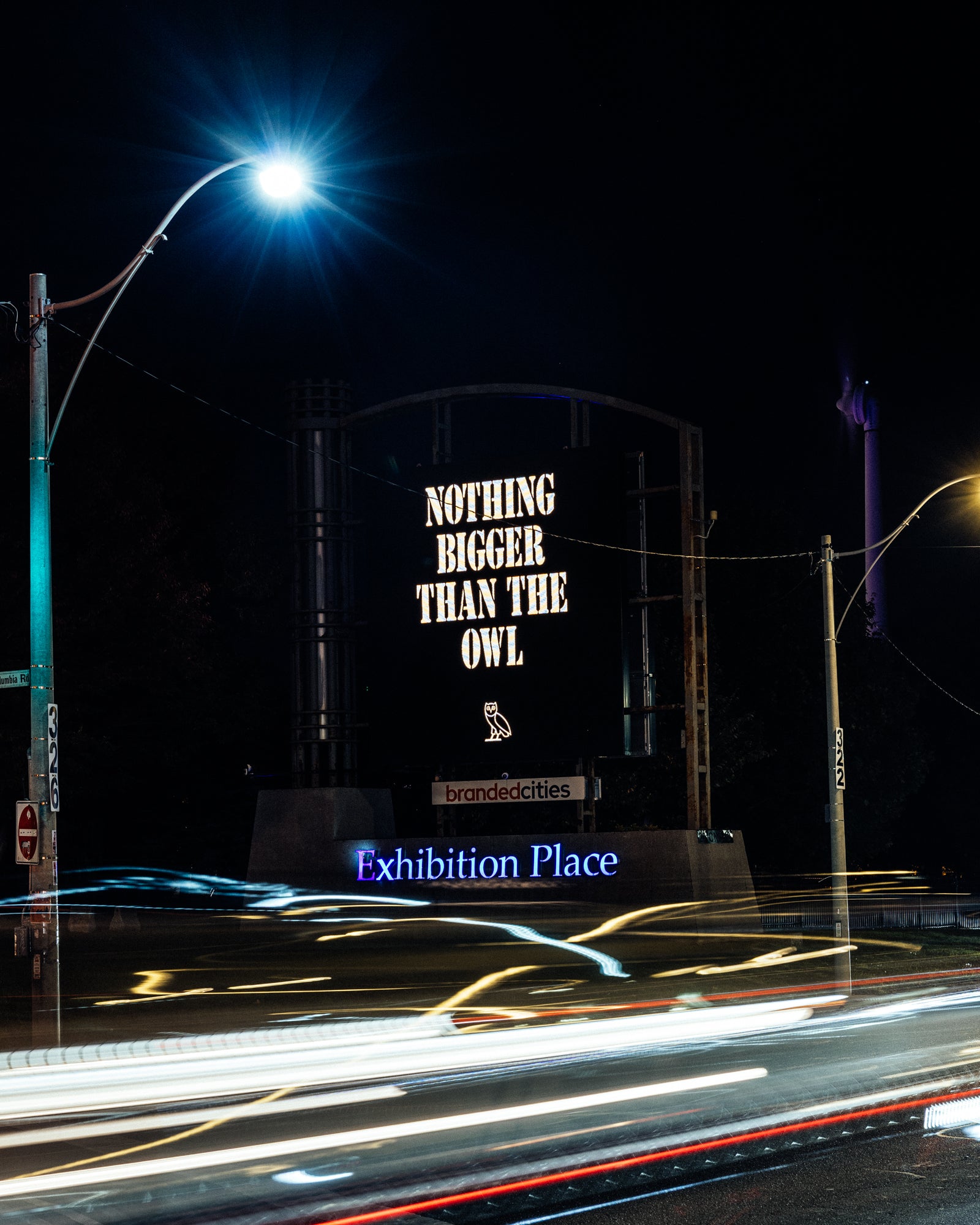 Billboard with 'Nothing Bigger Than The Owl' text at night, illuminated by streetlights.