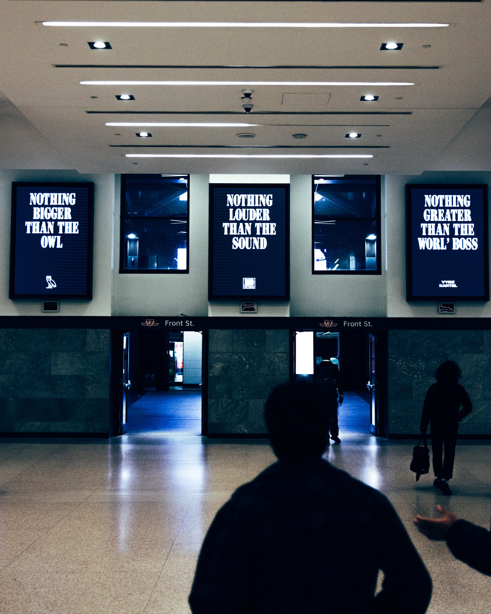 People walking through a terminal with large screens displaying motivational phrases.