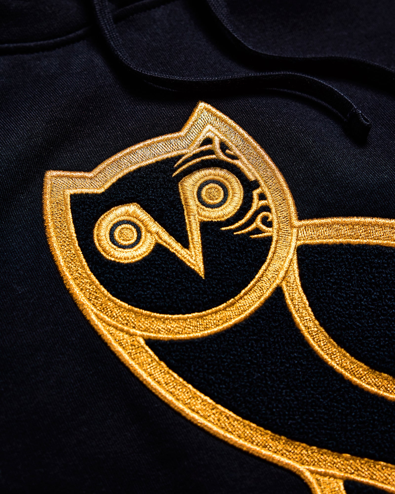 Close-up of a gold October's Very Own embroidered logo on a black fabric background