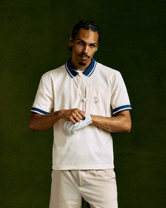 Cream polo shirt with navy and white striped collar and sleeve trim, featuring small chest logo.