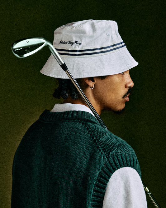 White bucket hat with navy stripe trim and embroidered text, worn with golf club visible.