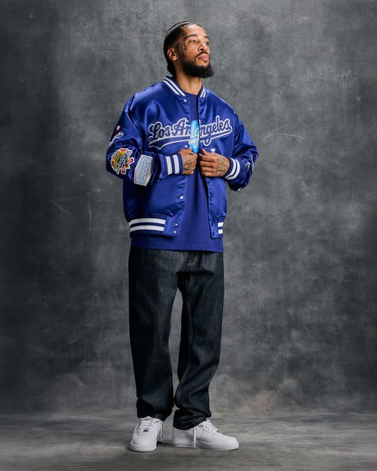 Blue varsity jacket with "Los Angeles" script across chest, white striping on sleeves and hem, and embroidered team patches o
