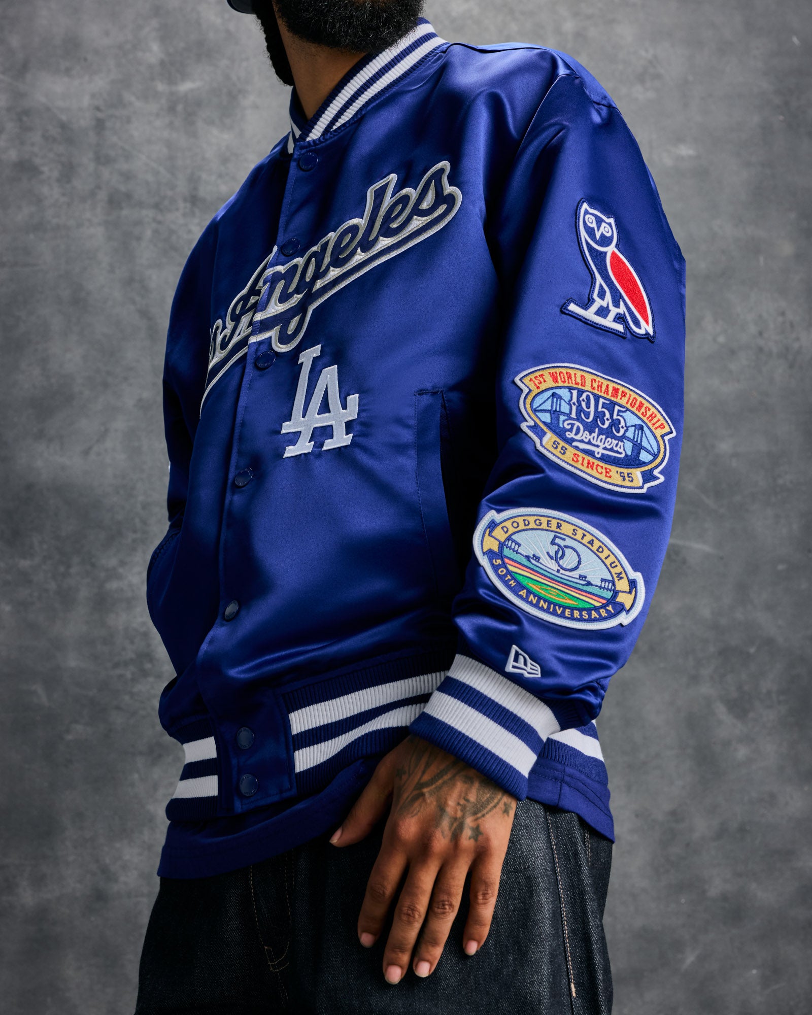 Blue varsity jacket with "Dodgers" and "LA" embroidery, striped ribbing, and championship patches on sleeves.