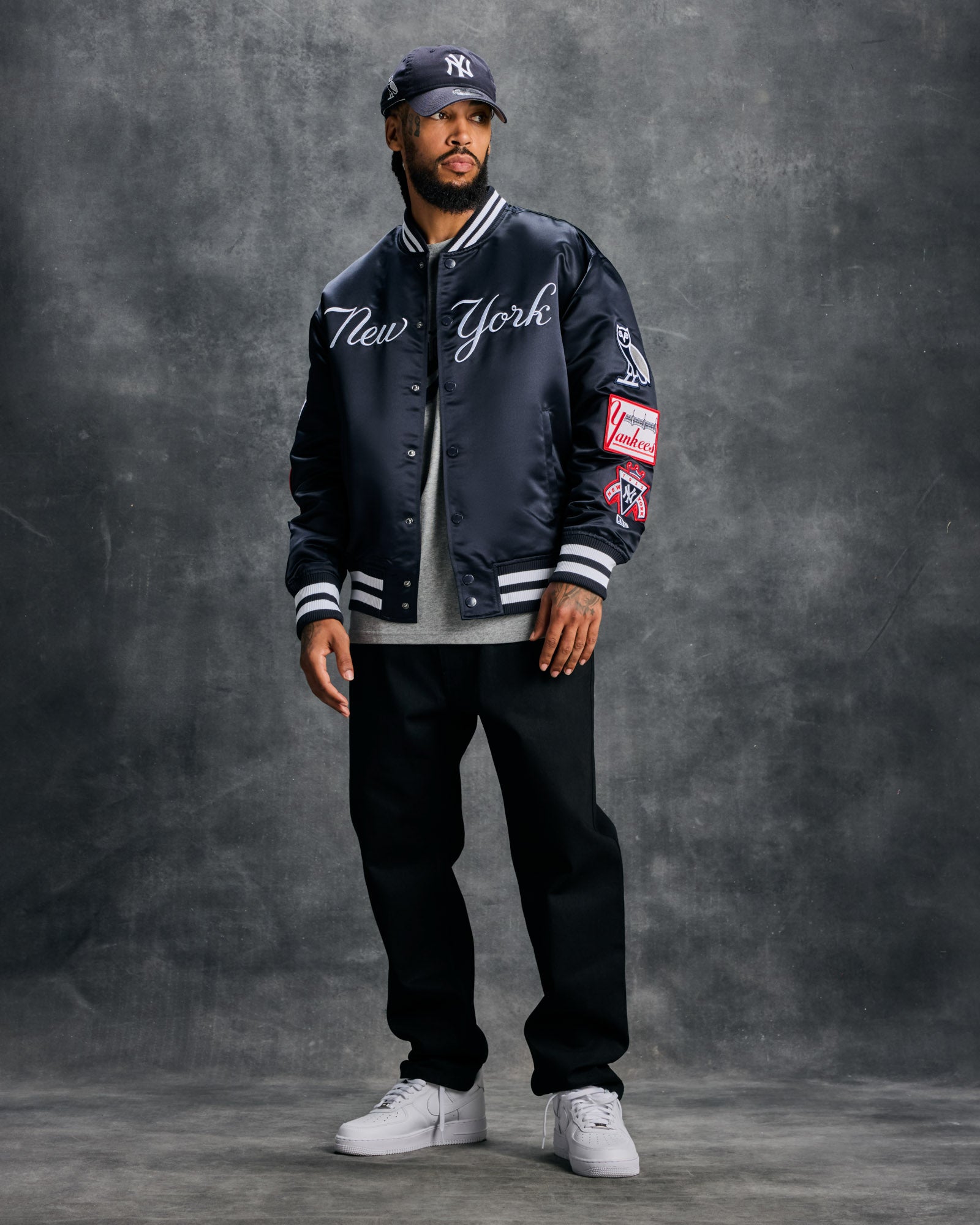 Navy varsity jacket with "New York" script across chest, white striped ribbing, and team patches on sleeves.
