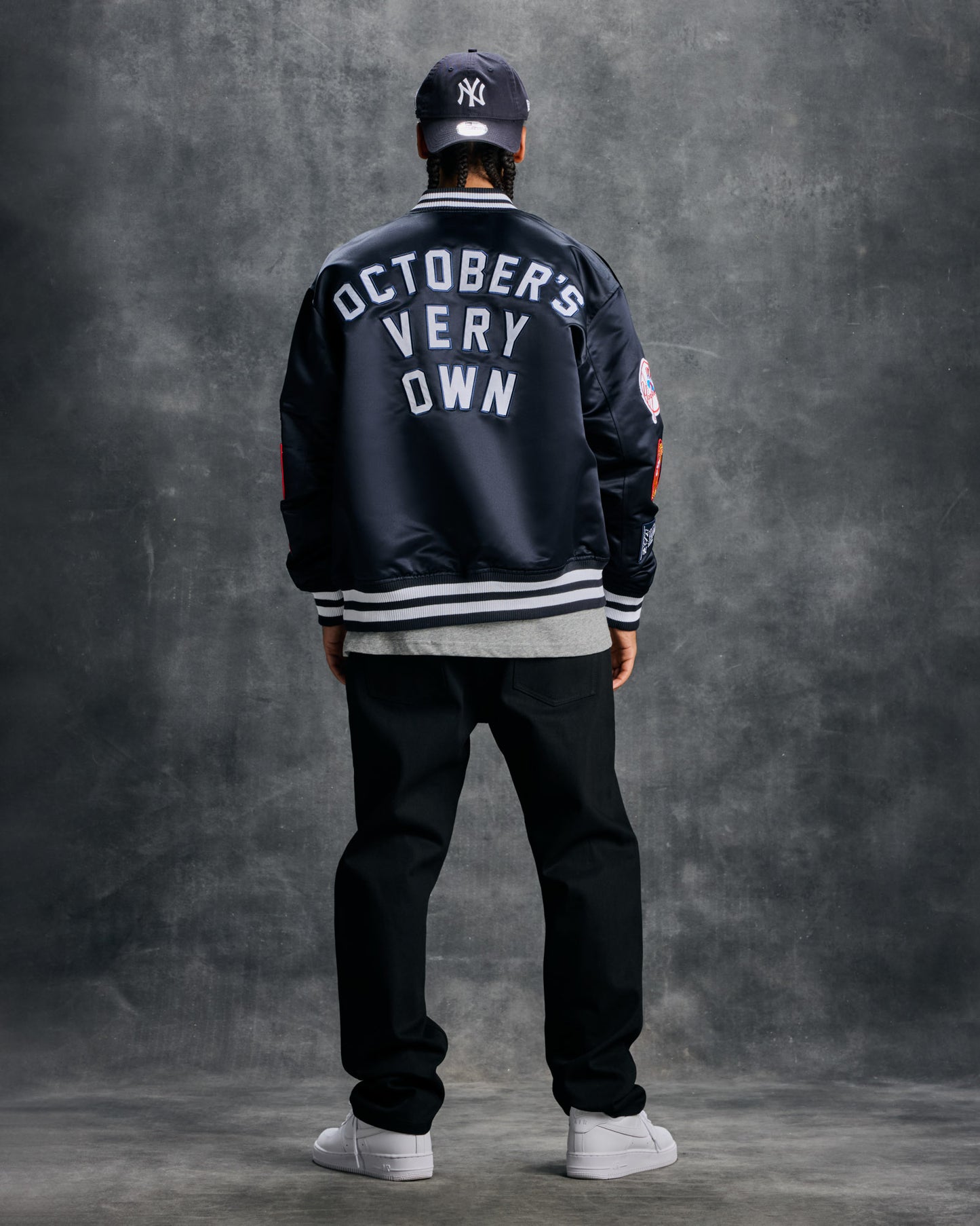Navy varsity jacket with "October's Very Own" text on back, white striped ribbing, and MLB logo patch, worn with matching cap