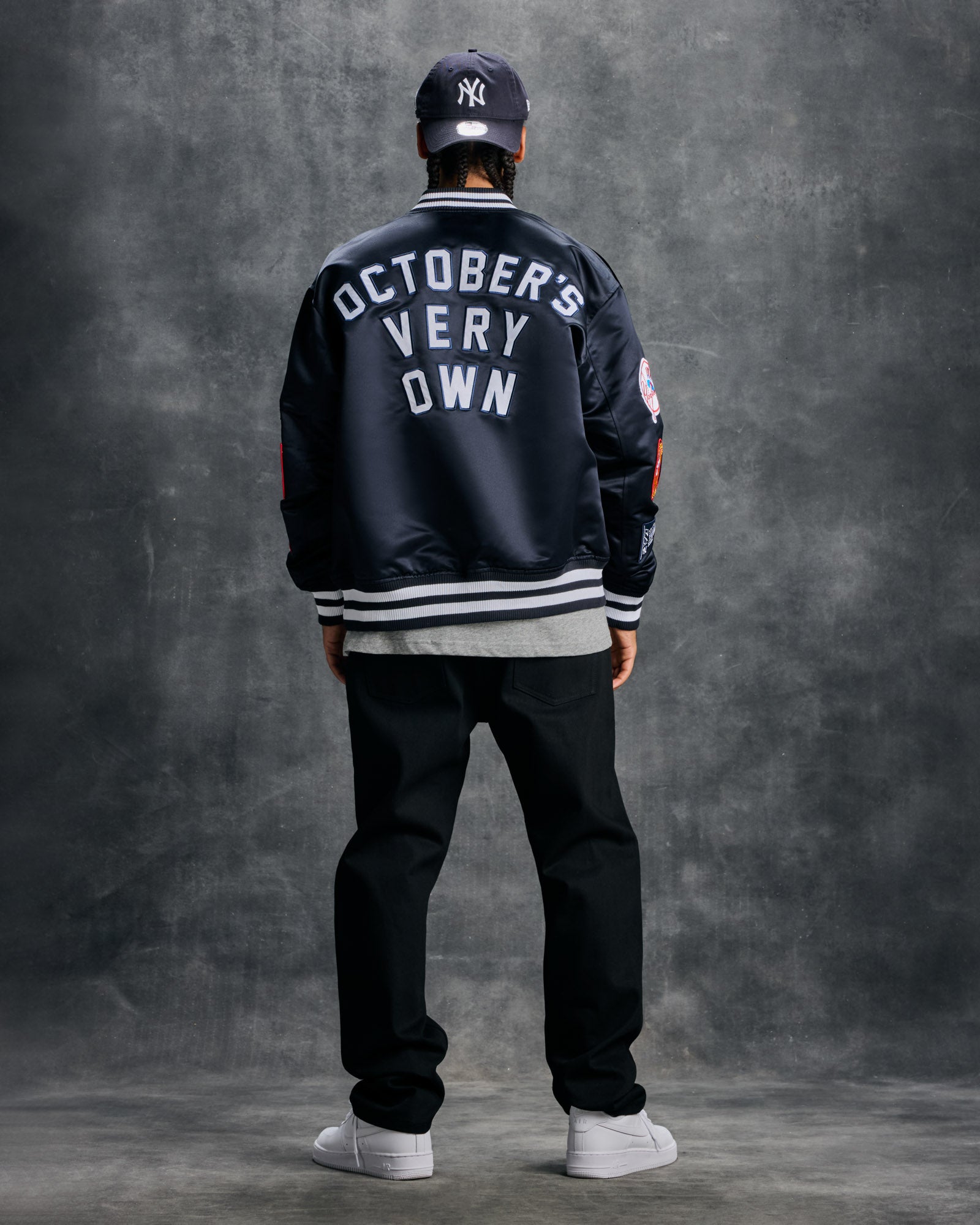 Navy varsity jacket with "October's Very Own" text on back, white striped ribbing, and MLB logo patch, worn with matching cap